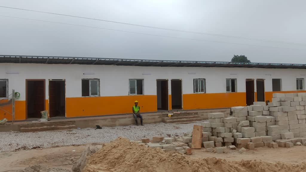 Construction de la base vie : bâtiments longs aux façades blanches et orange, fondations, clôture et chantier en cours — vue 3